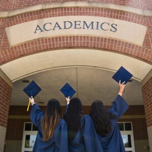 three girls in graduation gowns hold their caps in the air